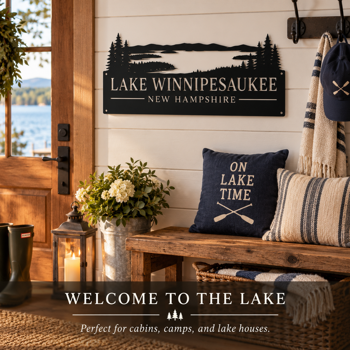 A decorative black metal sign reading “LAKE WINIPESAUKEE NEW HAMPSHIRE” hangs on a white shiplap wall above a rustic wooden bench. The scene includes a navy pillow that says “ON LAKE TIME,” woven cushions, a lantern, flowers, and a view of the lake through a doorway.