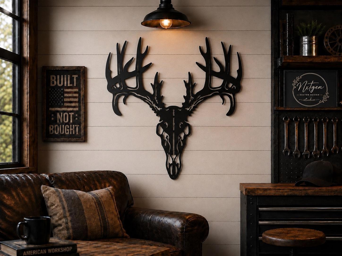 A black metal deer skull with large antlers mounted on a beige shiplap wall in a rustic room setting with a brown leather sofa, a hanging lamp, and a wooden cabinet.