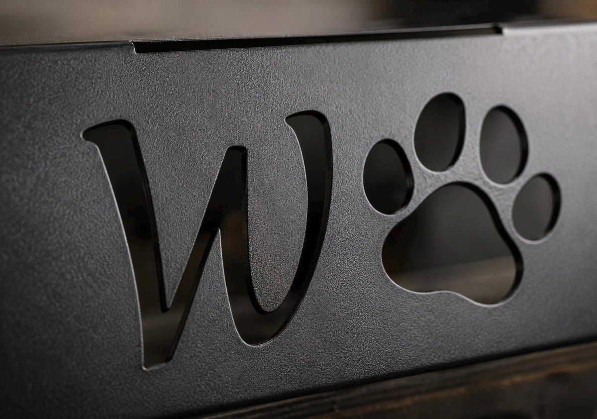 Close-up of a dark metal decorative piece featuring a large letter W and a paw print cutout, with a textured matte finish.