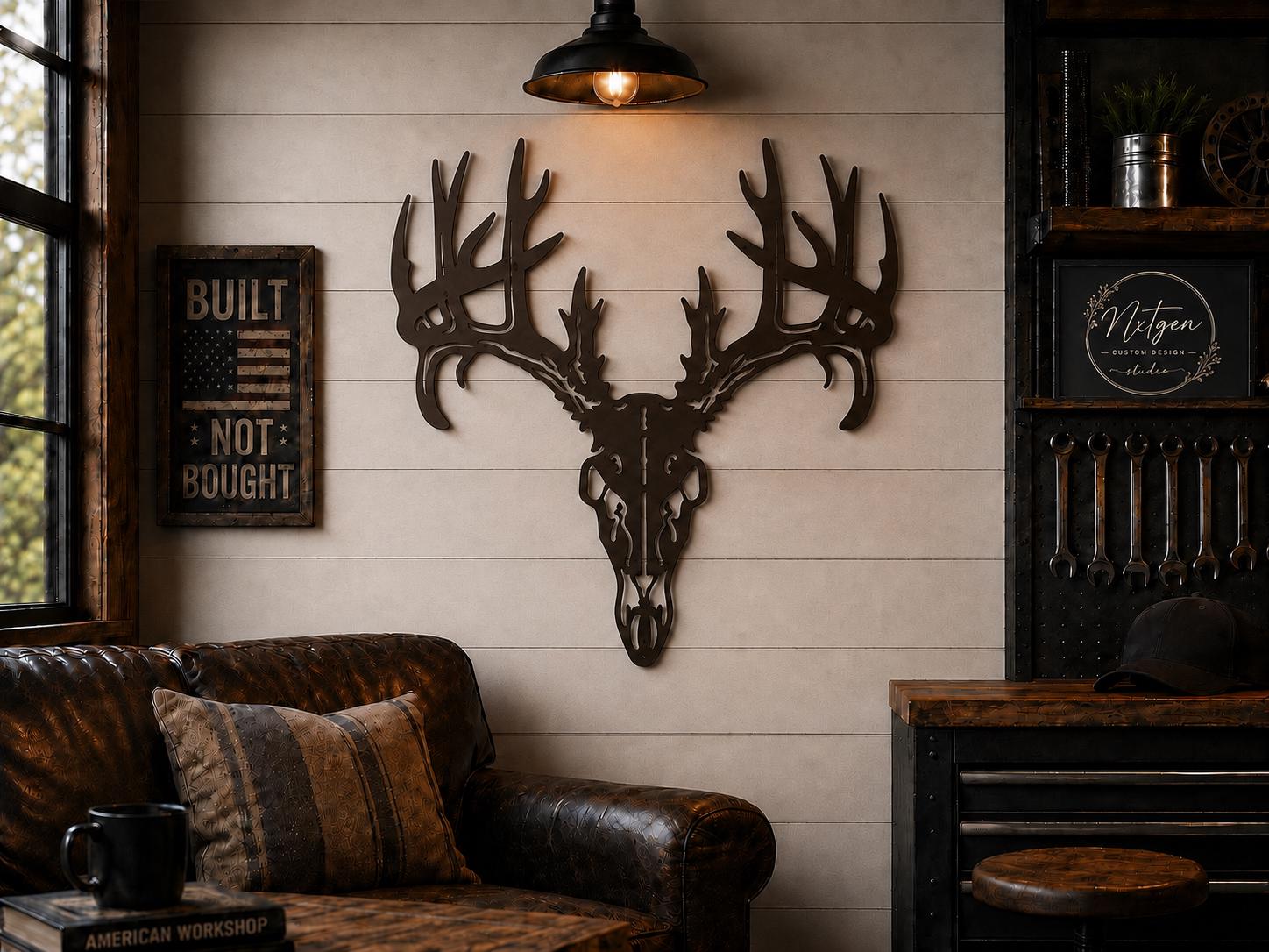 A rustic metal deer skull with large antlers mounted on a beige shiplap wall in a cabin-style room. A brown leather sofa with patterned pillows sits below, and a black pendant light hangs above.